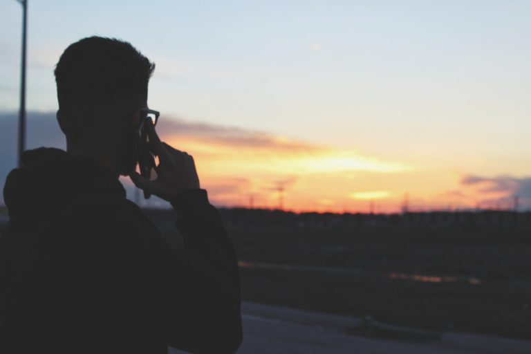 man using phone near road during daytime