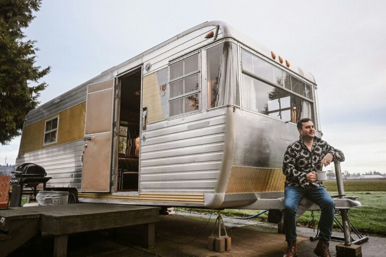 A man sitting beside a vintage travel trailer outdoors