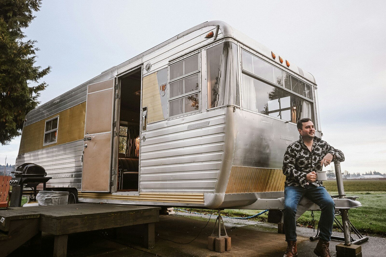 A man sitting beside a vintage travel trailer outdoors